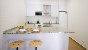 A modern kitchen with white cabinetry, a granite countertop, a microwave, a stove, and two wooden stools. - Comfortable getaway in Medieval Castro Marim by Lisbeyond (Castro Marim)