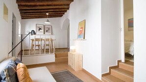 A compact living space with a wooden ceiling, a dining area with chairs and a table, a bed with pillows, and a staircase leading to another room. - Comfortable getaway in Medieval Castro Marim by Lisbeyond (Castro Marim)