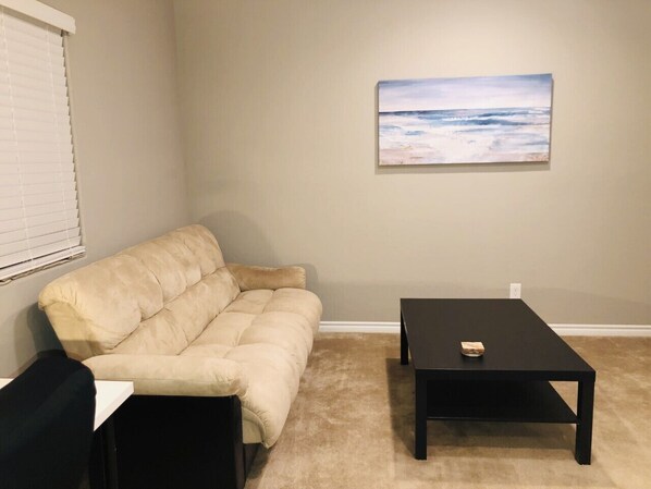 A living room with a beige sofa, a black coffee table, and a painting on the wall.