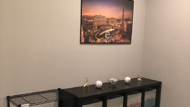 Um corredor com um console preto, uma estante aramada e uma imagem emoldurada de paisagem urbana na parede.