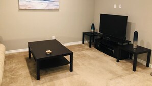 Uma sala de estar com televisão de tela plana, mesa de centro e um quadro na parede.