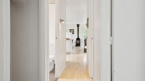 A narrow hallway with a wooden floor leading to a room with a black wood-burning stove. - 3 bedroom amazing home in Børkop (Børkop)