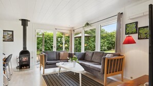A cozy living room with a fireplace, a sofa, a coffee table, and a view of greenery outside. - 3 bedroom amazing home in Børkop (Børkop)