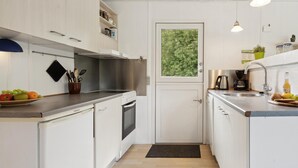 A compact kitchen with white cabinetry, a stainless steel range hood, a built-in oven, a sink with a faucet, and a window with a view of greenery. - 3 bedroom amazing home in Børkop (Børkop)