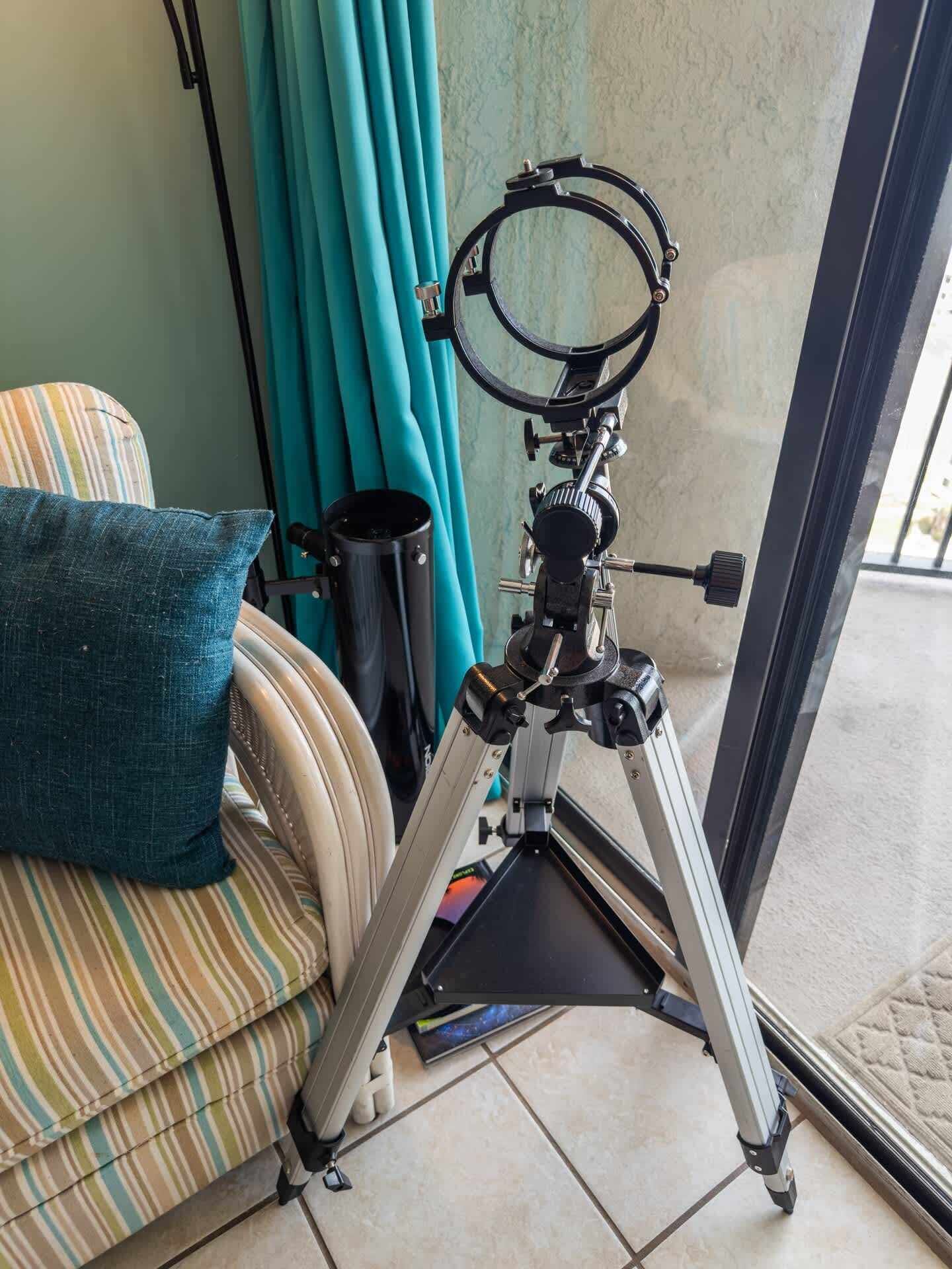A telescope on a tripod in a room with a sofa and curtains.