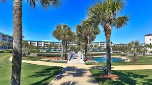 A pathway leading to a building with a pool, surrounded by palm trees and a well-maintained lawn. - Steps from the Beach ~ 1st floor w/ pool view~ Amalfi Coast (Miramar Beach)