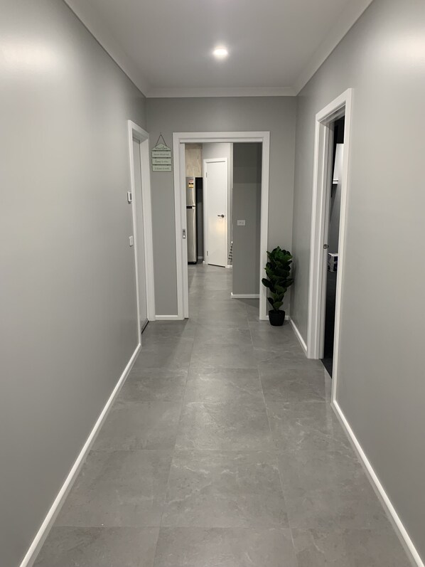 A hallway with grey walls and a grey tiled floor, leading to a door at the end.