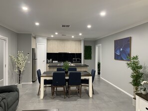 A modern kitchen with black countertops, a dining area with a wooden table and chairs, and a grey living room with a sofa.