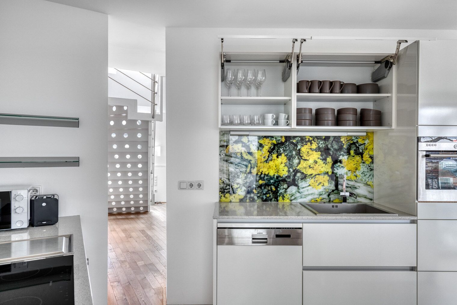Una cocina moderna con armarios blancos, horno empotrado y salpicadero con estampado floral amarillo.