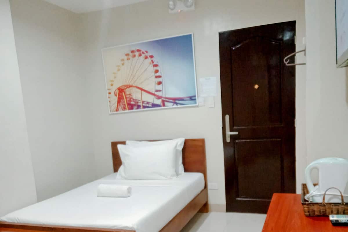 Una habitación pequeña y ordenada con una cama, una mesa de madera y un cuadro en la pared de una noria.