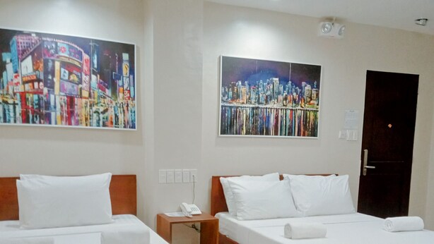 A hotel room with two beds, a wooden bench, a nightstand with a phone, and two paintings on the walls. - Grace & RB Hotel (Kalibo)