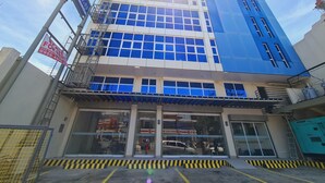 A multi-story building with large windows, a blue facade, and a sign indicating it is for rent. - Grace & RB Hotel (Kalibo)