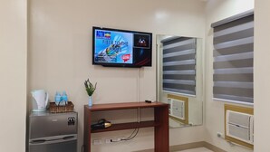 A hotel room with a kitchenette, a television mounted on the wall, a mirror, and a window with blinds. - Grace & RB Hotel (Kalibo)