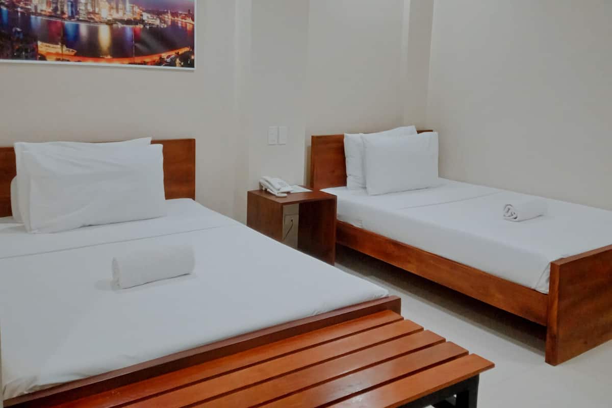 Habitación de hotel con dos camas individuales, un banco de madera, una mesita de noche con teléfono y un cuadro de paisaje urbano en la pared.