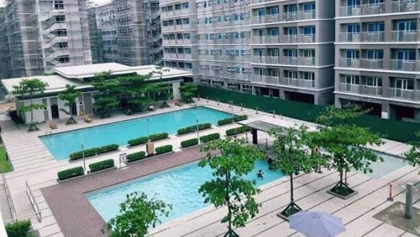 A modern multi-story hotel with a central swimming pool surrounded by greenery and outdoor seating areas. - Stylish 1BR Retreat at Trees Residences — Fast WiFi, Smart TV, Near SM Fairview (Quezon City)