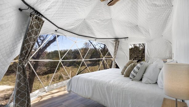A tented accommodation with a bed, curtains, and a view of the outdoors.