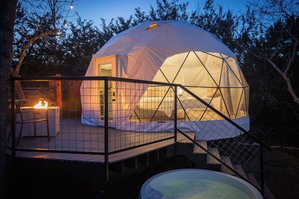 A dome-shaped tent with a covered deck and a hot tub in front.