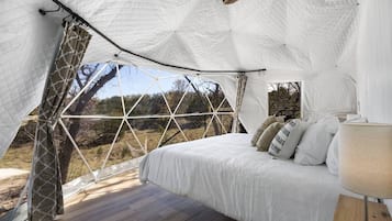 Alojamiento en tienda de campaña con cama, cortinas y vistas al exterior.