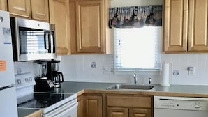 A kitchen with wooden cabinets, a stainless steel refrigerator, a microwave, a stove, a dishwasher, and a window with curtains.