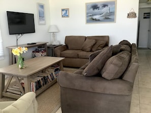 Una sala de estar con un sofá marrón, un televisor, una mesa con libros y un jarrón de flores.