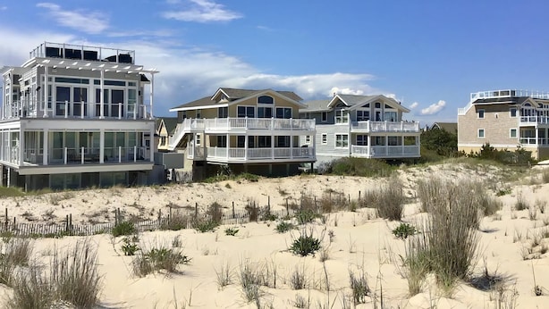 A beachfront property with multiple-story houses, large windows, and a sandy landscape.