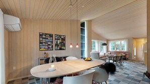 A modern dining area with a wooden ceiling, a large table, white chairs, and a patterned rug. - Beautiful house, 1st row to the water (Fur)
