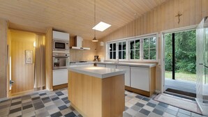 A modern kitchen with wooden walls, a central island, and a large window. - Beautiful house, 1st row to the water (Fur)