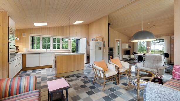 A spacious living area with a checkered floor, wooden walls, a kitchen with a large window, and a dining area with chairs and a table. - Beautiful house, 1st row to the water (Fur)