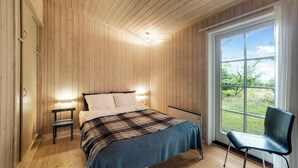 A wooden-paneled bedroom with a bed, bedside lamps, a chair, and a large window. - Beautiful house, 1st row to the water (Fur)