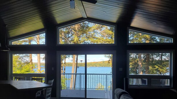 A spacious room with a large sliding glass door leading to a deck overlooking a lake, surrounded by trees. - Where Friends and Family make Memories. (South River)