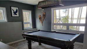 A pool table in a room with two windows, a framed eagle picture, and a sign above the table. - Where Friends and Family make Memories. (South River)