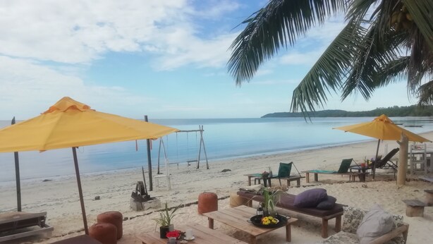 Un espacio de descanso en la playa con mobiliario de madera, sombrillas amarillas y vistas al mar.