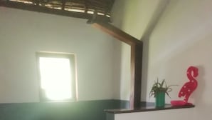 Un pasillo con pared verde y blanca, un banco de madera, una planta en maceta y un adorno rojo.