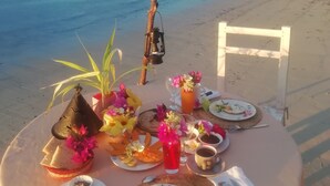 Mesa en la playa dispuesta con comida y bebidas, con vista al océano.