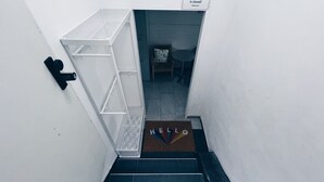 A stairwell with a white wall, a metal handrail, a door with a 'HELLO' mat, and a 'SNOKI' sign on the wall.