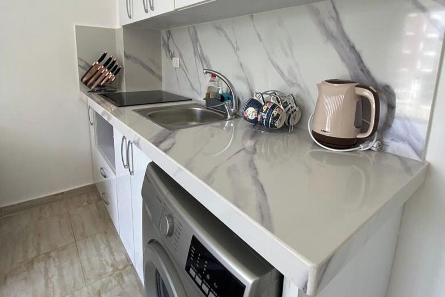 Una cocina compacta con encimera de mármol, lavavajillas integrado, un lavabo y una cafetera.