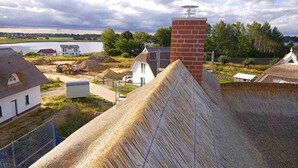 Landligt miljø med et stråtækt hus, en murstens skorsten og et vandareal i baggrunden.