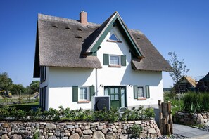 Une maison à deux étages, avec un toit de chaume, des murs extérieurs blancs et des volets verts.