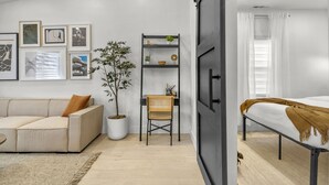 A modern bedroom with a bed, a desk, and a chair. There is a bookshelf with books and decorative items. A potted plant is on the floor next to the desk. - Private Luxury Tiny Home (Dearborn Heights)