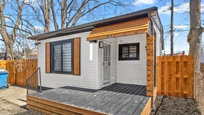 A small, single-story cabin with a wooden deck, a fenced backyard, and a clear sky. - Private Luxury Tiny Home (Dearborn Heights)