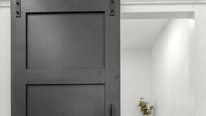 A sliding barn door in a room with a wooden cabinet and a woven basket. - Private Luxury Tiny Home (Dearborn Heights)