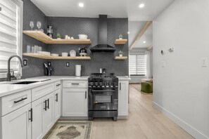 Une cuisine moderne avec des meubles blancs, une cuisinière noire et des étagères en bois.