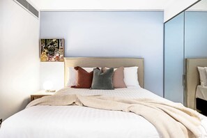 A neatly made bed with a beige blanket, a headboard, and several pillows.