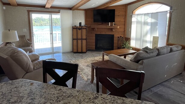 A spacious living area with a fireplace, a television, and a large window overlooking a scenic view. - Waterfront Bungalow nightly panoramic view of our illuminated covered Bridge (Galloway)