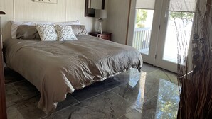 A bedroom with a large bed, a nightstand, a mirror, and a window with blinds. - Waterfront Bungalow nightly panoramic view of our illuminated covered Bridge (Galloway)