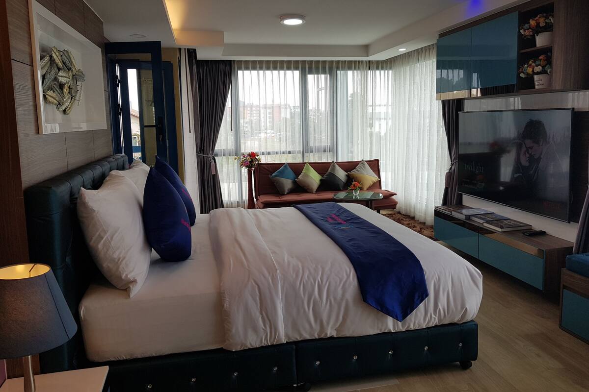 A modern hotel room with a large bed, a TV, and a balcony with curtains.