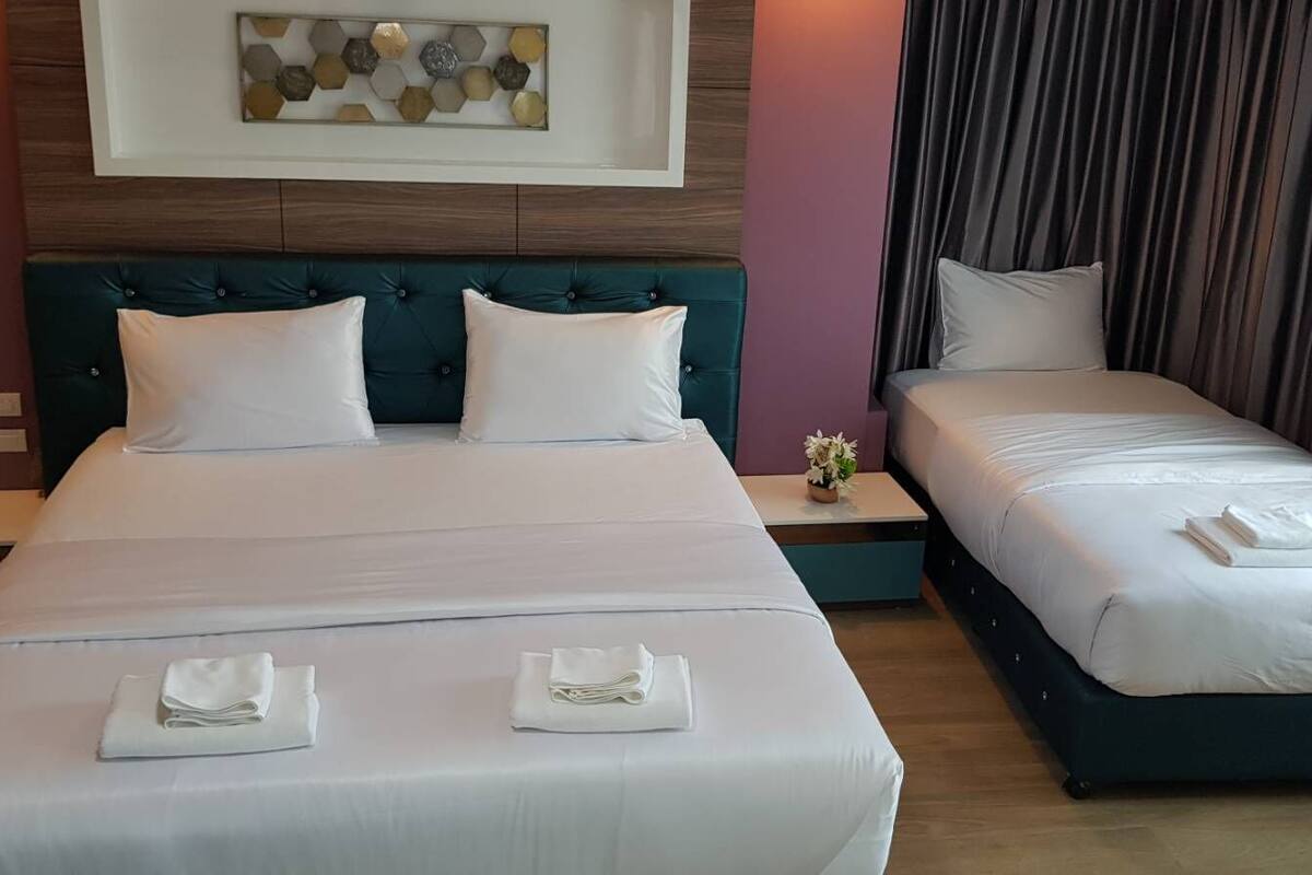 A hotel room with a large bed, a smaller bed, and a nightstand with a vase of flowers.