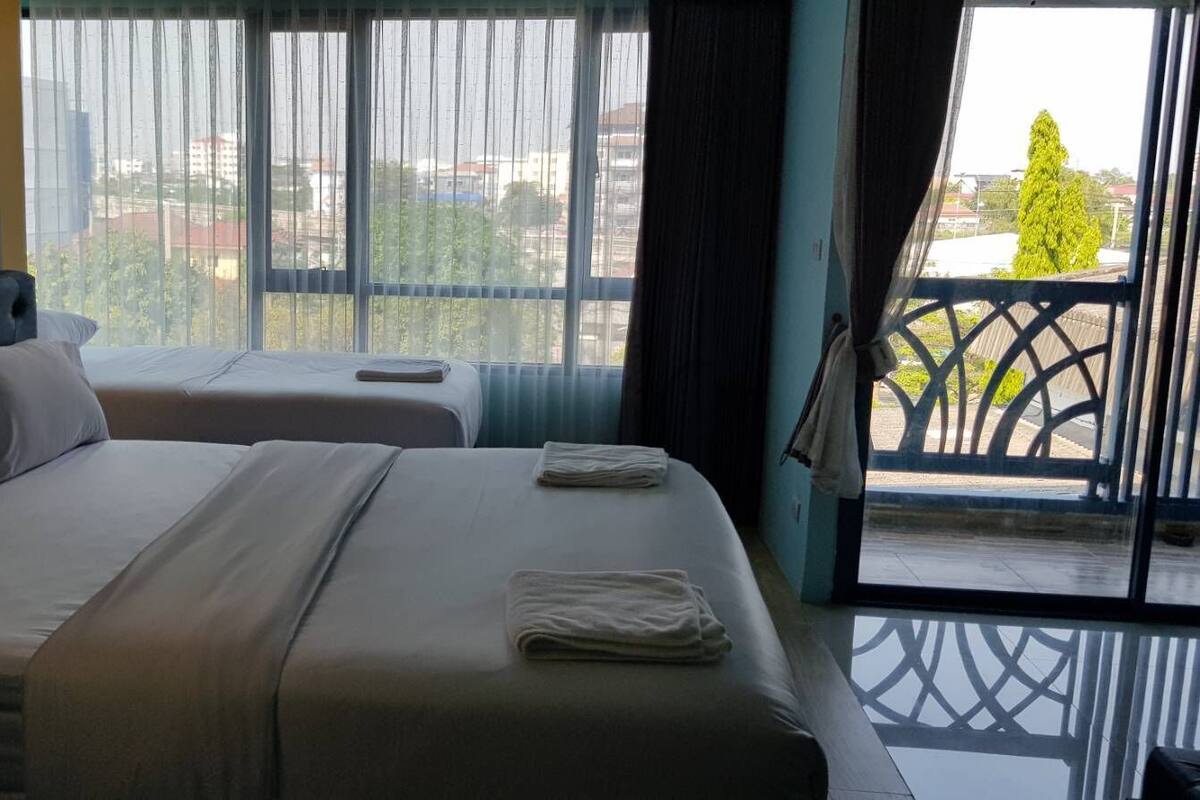 A hotel room with two beds, a view of the city through large windows, and a balcony with a railing.