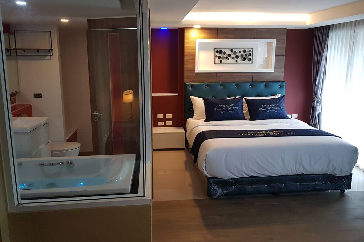 A modern hotel room with a large bed, a glass-enclosed shower, and a wall-mounted artwork.