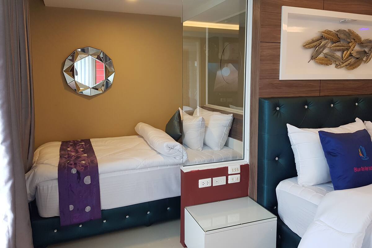 A hotel room with a bed, a bedside table, a mirror, and a wall-mounted artwork.